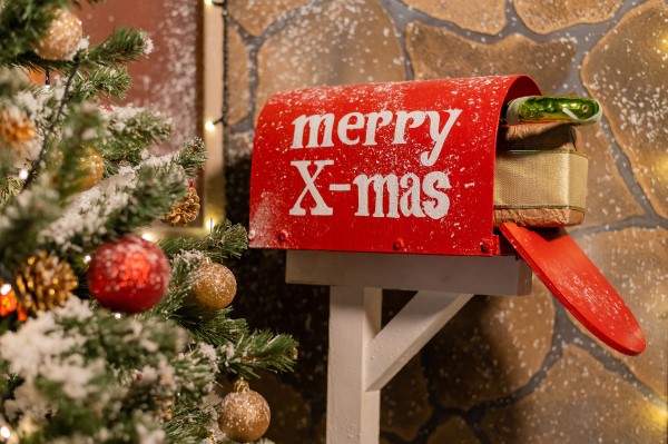 festive scene showing a an open post box with 'merry X-mas' written on it and parcels inside next to a Xmas tree